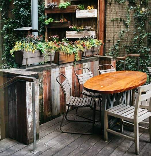 Wooden patio with a table, chairs, and a wall-mounted planter filled with flowers.