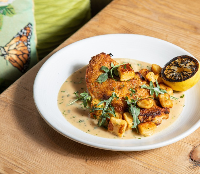 A plated dish with chicken, roasted potatoes, and a creamy sauce garnished with herbs.