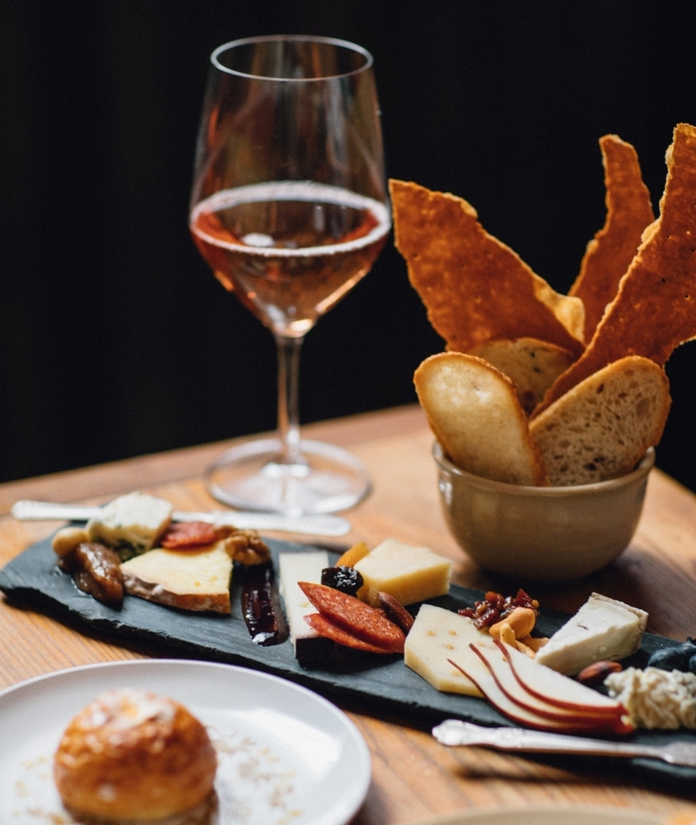 A charcuterie board with bread, meats, and cheeses pairs with a glass of rosé wine.