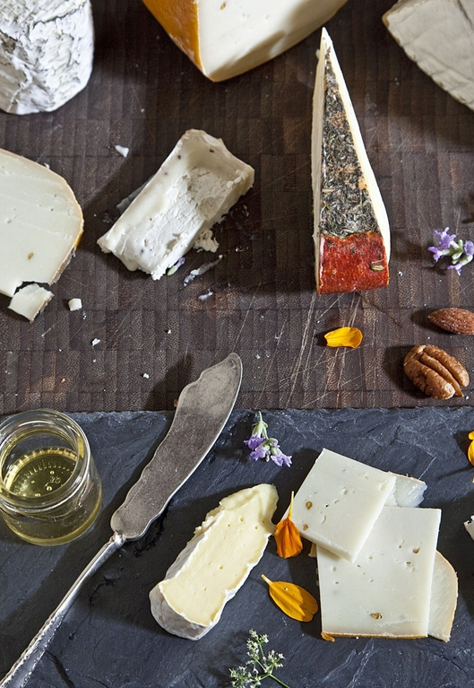 Assorted cheeses on slate board with almonds, honey, and lavender, showcasing a gourmet cheese platter.