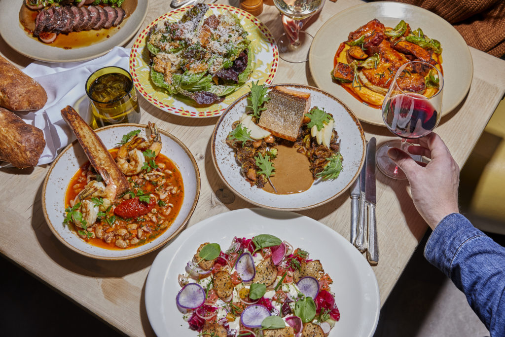 Hand holding a glass of wine at a table full of a variety of entrees